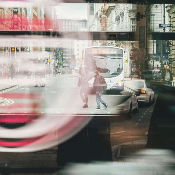 An image of a blurred city shot with a bus going by in the foreground and people walking in the background of the bus window